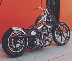 a black and silver motorcycle parked in front of a red building with an orange wall