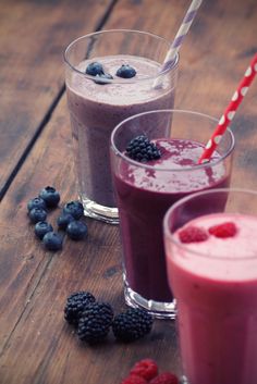 two glasses filled with smoothies next to berries