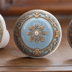 three decorative blue and gold knobs on top of a wooden table with white handles