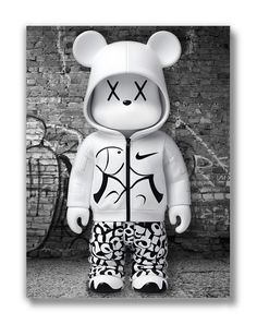 a black and white photo of a teddy bear in front of a wall with graffiti