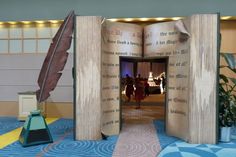 an open book sitting on top of a blue floor next to a feather quill