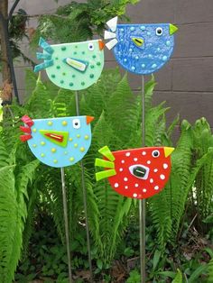 three colorful birds on top of metal poles in front of some plants and trees with green leaves