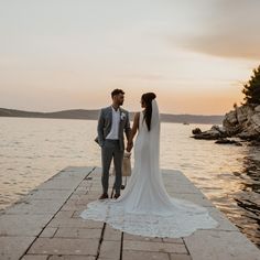 a bride and groom standing on a dock holding hands at the end of their wedding day