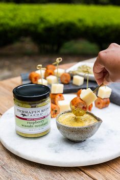 a person dipping cheese on skewers into a bowl with mustard and other toppings