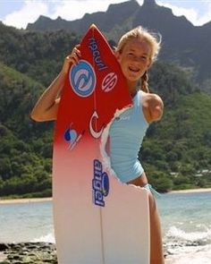 a woman standing on the beach holding a surfboard with mountains in the back ground