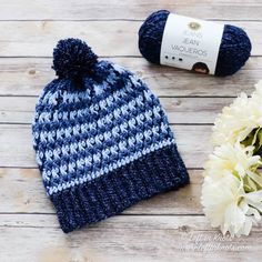 a crocheted blue and white hat sitting next to a ball of yarn on top of a wooden table