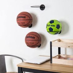 three basketballs are hanging on the wall next to a chair and table with a laptop