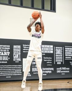 a young man holding a basketball on top of a gym floor in front of a wall