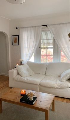 a living room with a white couch and table in front of the large window that has curtains on it