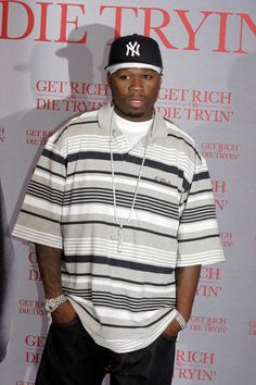 a man standing in front of a wall wearing a baseball cap and striped shirt with his hands on his hips