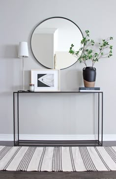 a black and white table with a mirror on it next to a plant in a vase