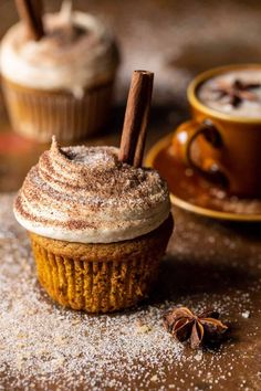 two cupcakes on a table with cinnamon sticks sticking out of them