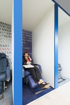 a woman sitting at a table in an office with blue chairs and wallpaper behind her