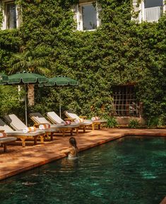 a pool with lounge chairs and an umbrella in front of a large green ivy covered building