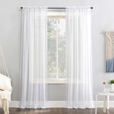 a white curtain hanging in front of a window next to a chair and table with a potted plant on it