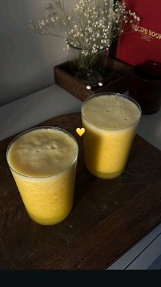 two glasses filled with yellow liquid sitting on top of a wooden table