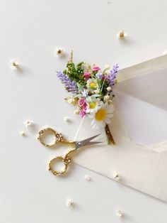 a pair of scissors and some flowers on a white surface with tiny beads around it