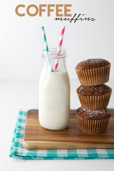 three muffins on a cutting board next to a glass of milk and two straws