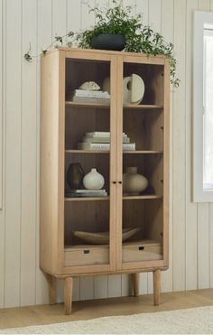 a wooden cabinet with glass doors and plants on top in a room that has white walls