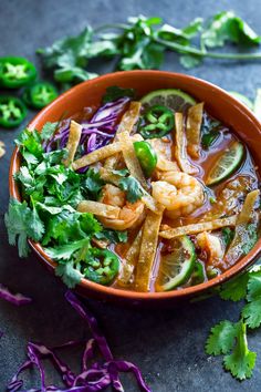 a bowl filled with shrimp and vegetables next to cilantro, lime wedges