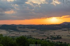 the sun is setting over rolling hills and trees in the foreground, with an orange sky