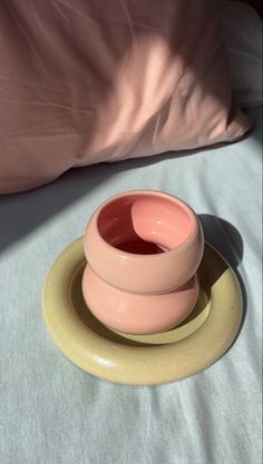 a small pink bowl sitting on top of a yellow plate next to a white pillow