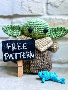 a crocheted baby yoda holding a sign with the word free pattern next to it