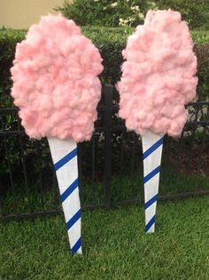 two pink cotton candy cones sitting on top of green grass next to a black fence