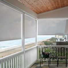 a porch with white blinds and a bench on the front porch overlooking the beach in the background