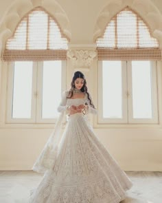 a woman in a white wedding dress standing next to two windows