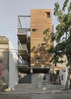 an apartment building with stairs leading up to the top floor and two people sitting on a bench in front of it