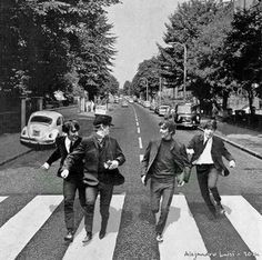 the beatles crossing the street in front of an old car and some people walking across it