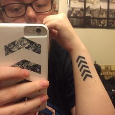 a woman taking a selfie in front of her phone with an arrow tattoo on her arm