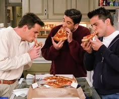 three men are eating pizza in the kitchen