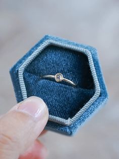 a hand holding a ring in a blue velvet box with a diamond on the top