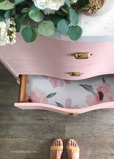 a pair of pink shoes sitting on top of a wooden dresser next to flowers and greenery