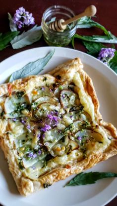 there is a piece of pizza on the plate next to flowers and a honey jar