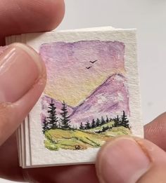 a person holding a small card with a painting on it