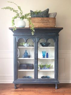 a blue china cabinet with glass doors and shelves filled with vases, plants and other decorative items