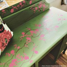 a green bench with pink flowers painted on the top and bottom, sitting in front of a mirror