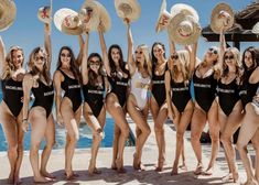 a group of women standing next to each other in bathing suits and hats on the beach