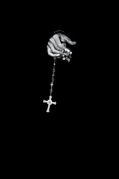 a black and white photo of a person's hand holding a chain with a cross on it