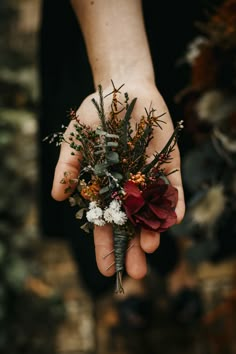 a person's hand holding a flower bouquet in their left hand with other flowers on it