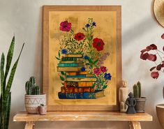 there is a painting on the wall with books and flowers in it next to some potted plants