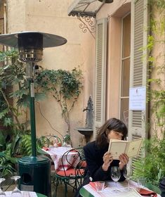 a woman sitting at an outdoor table reading a book