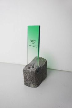 a rock with a green glass stand on it's side next to a white wall