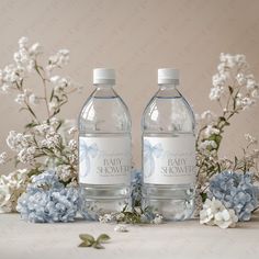 two bottled water bottles sitting on top of a table next to blue and white flowers