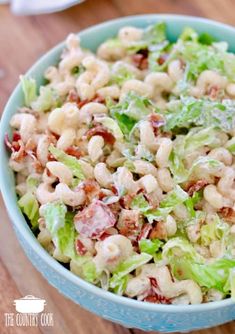 a salad with lettuce, bacon and cheese in a blue bowl on top of a wooden table