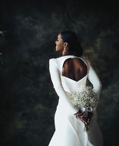 a woman in a white dress holding a bouquet of flowers and looking off into the distance