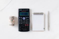 a calculator, notepad and pen sitting on a table next to each other